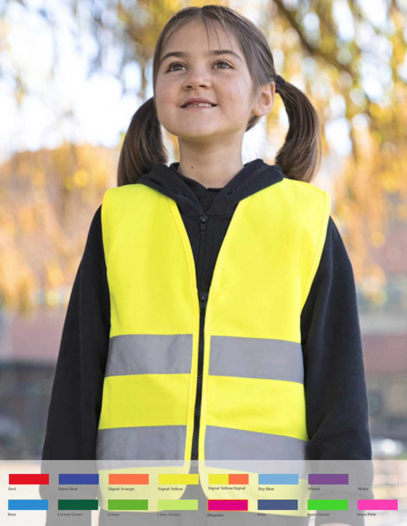 Jonge jongen met glimlach draagt felgele reflecterende veiligheidsjas, buiten met onscherpe herfstige achtergrond.